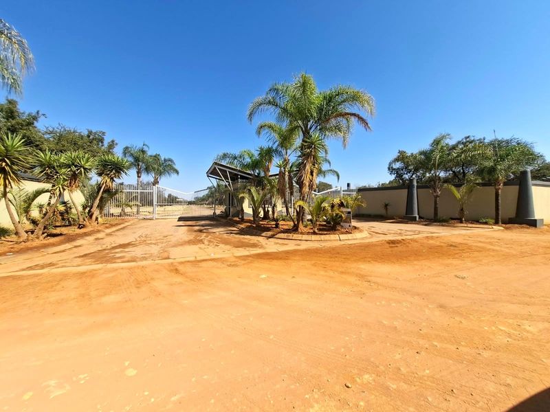 Front entrance view of a residential property featuring a security gate, perimeter wall, and established palm trees on a large plot.