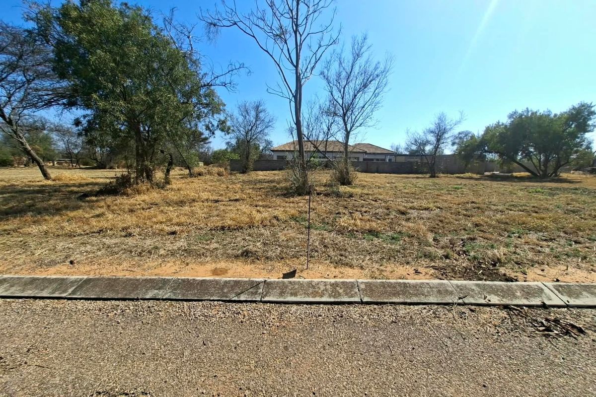 A vacant residential plot featuring natural vegetation, a concrete curb, and an asphalt road frontage, ready for development.