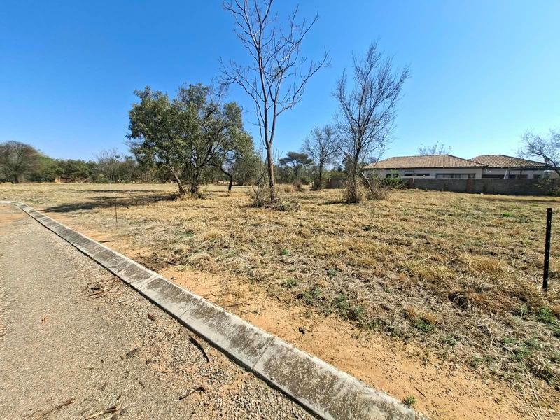 A vacant residential plot featuring a level landscape, concrete curbing, and an asphalt road frontage, ready for development.