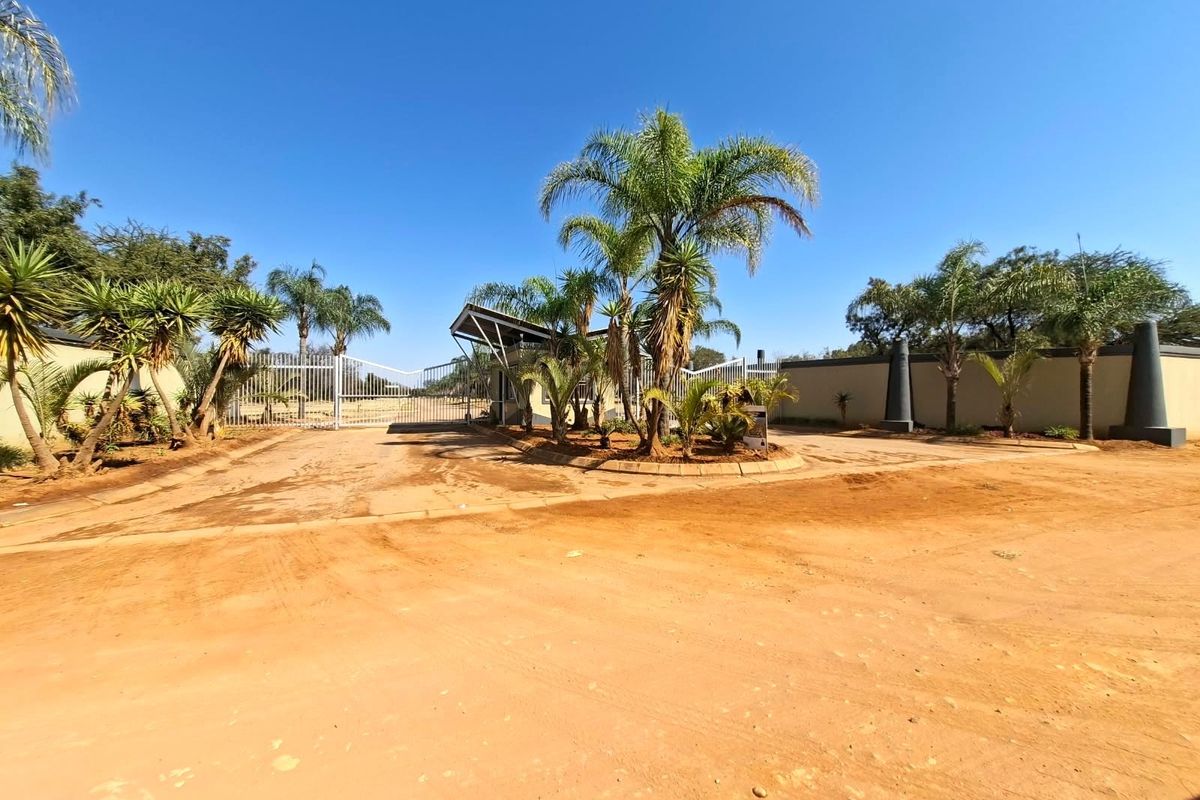 Front entrance view of a residential property featuring a security gate, perimeter wall, and established palm trees on a large plot.