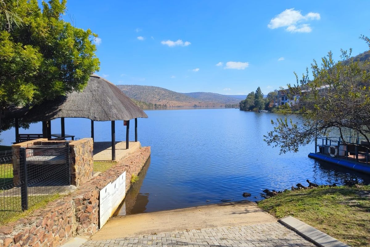 Scenic waterfront view featuring a thatched gazebo, stone retaining wall, and a paved boat launch ramp leading directly into the lake.