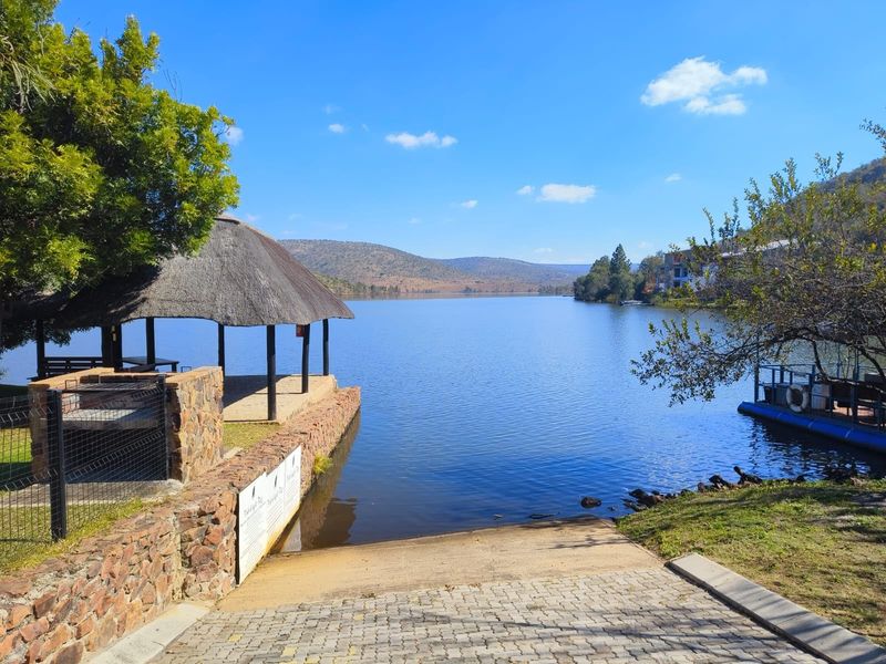 Scenic waterfront view featuring a thatched gazebo, stone retaining wall, and a paved boat launch ramp leading directly into the lake.