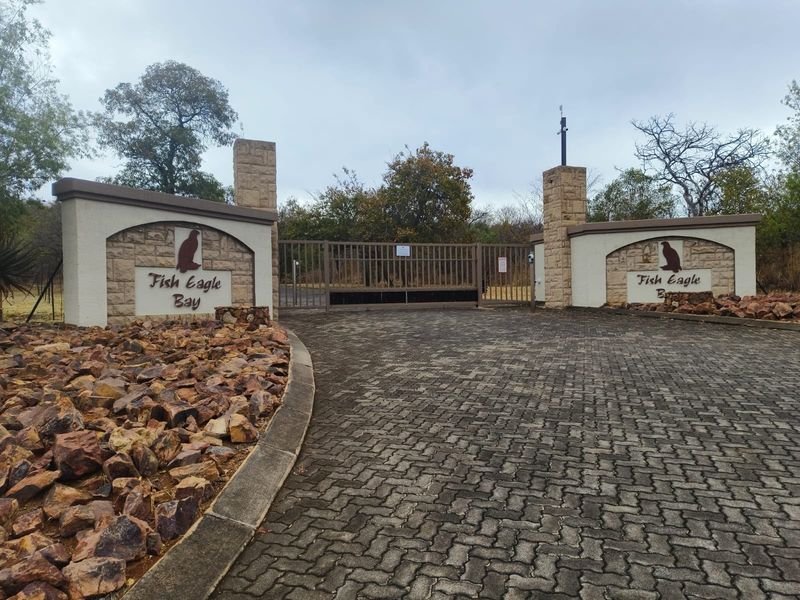 The secure gated entrance to Fish Eagle Bay, featuring stone masonry pillars, a paved driveway, and established landscaping.