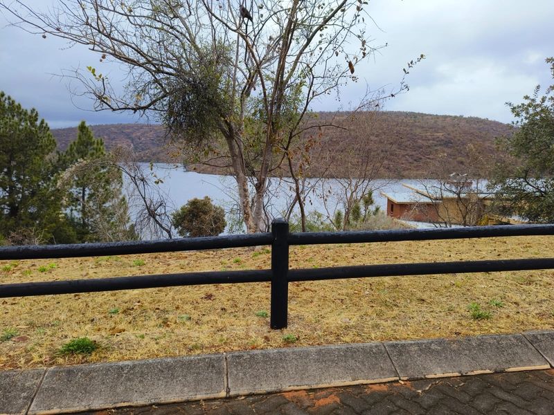 A scenic view overlooking a lake and surrounding hills, featuring a post and rail fence in the foreground.