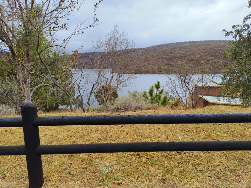 A scenic view overlooking a lake and surrounding hills, framed by a timber post and rail fence on the property.