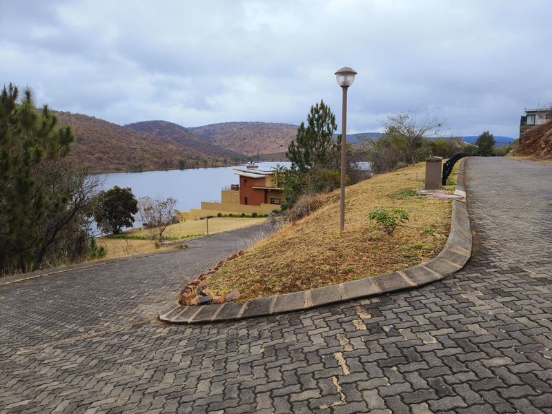 A scenic view overlooking a lake and surrounding hills, featuring a paved driveway and established street infrastructure within a residential estate.