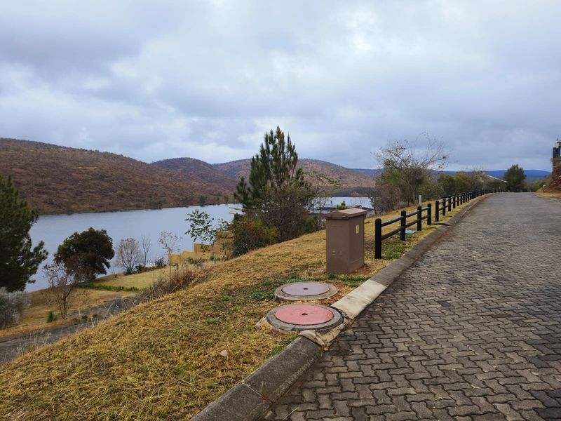A view of the paved street and verge area, featuring utility infrastructure and a scenic outlook over the nearby water and hills.