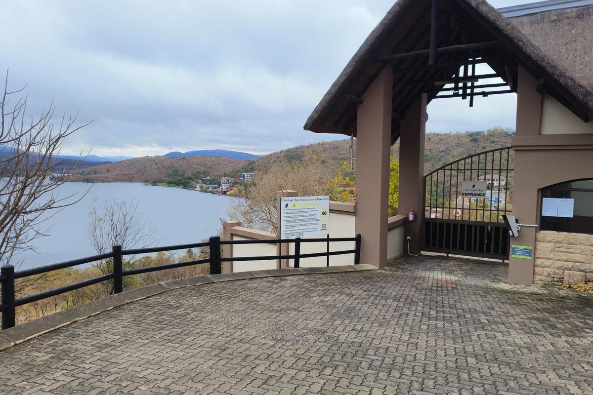 Entrance gate to the residential estate featuring a thatched roof structure, paved driveway, and scenic views of the adjacent lake and hills.