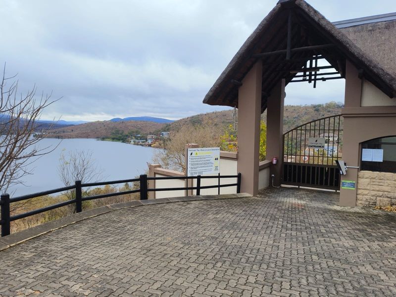 Entrance gate to the residential estate featuring a thatched roof structure, paved driveway, and scenic views of the adjacent lake and hills.
