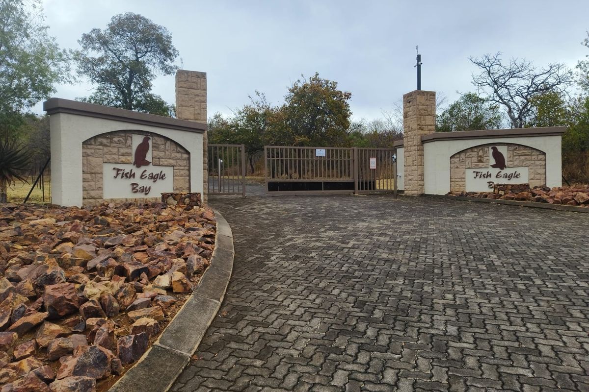 The entrance to Fish Eagle Bay featuring stone masonry pillars, a paved driveway, and a secure metal gate.