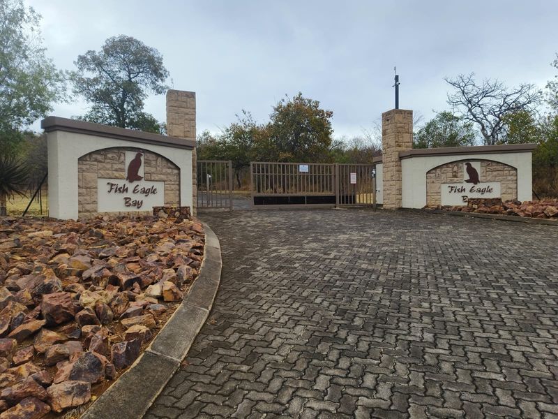 The entrance to Fish Eagle Bay featuring stone masonry pillars, a paved driveway, and a secure metal gate.