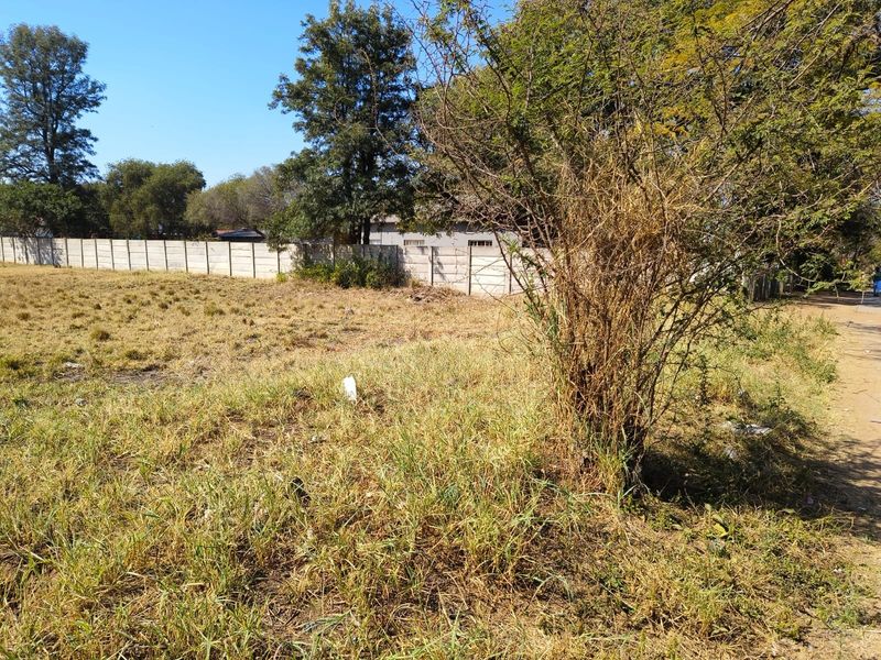 A view of a vacant residential plot featuring natural grass cover and a precast concrete boundary wall along the perimeter.