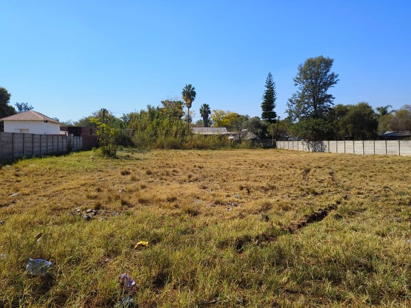 A vacant residential plot featuring dry grass and enclosed by precast concrete boundary walls, offering a blank canvas for future development.
