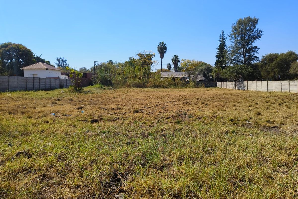 A vacant residential plot featuring dry grass and enclosed by precast concrete boundary walls on the sides.