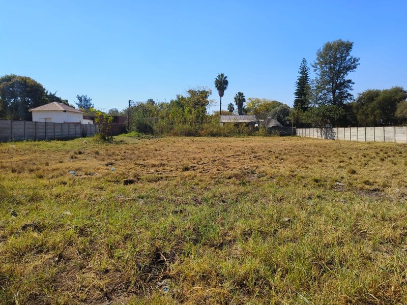 A vacant residential plot featuring dry grass and enclosed by precast concrete boundary walls on the sides.