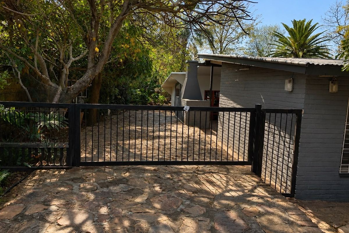 Rear exterior view featuring stone paving, a metal security gate, and a built-in outdoor fireplace adjacent to a brick-walled structure.