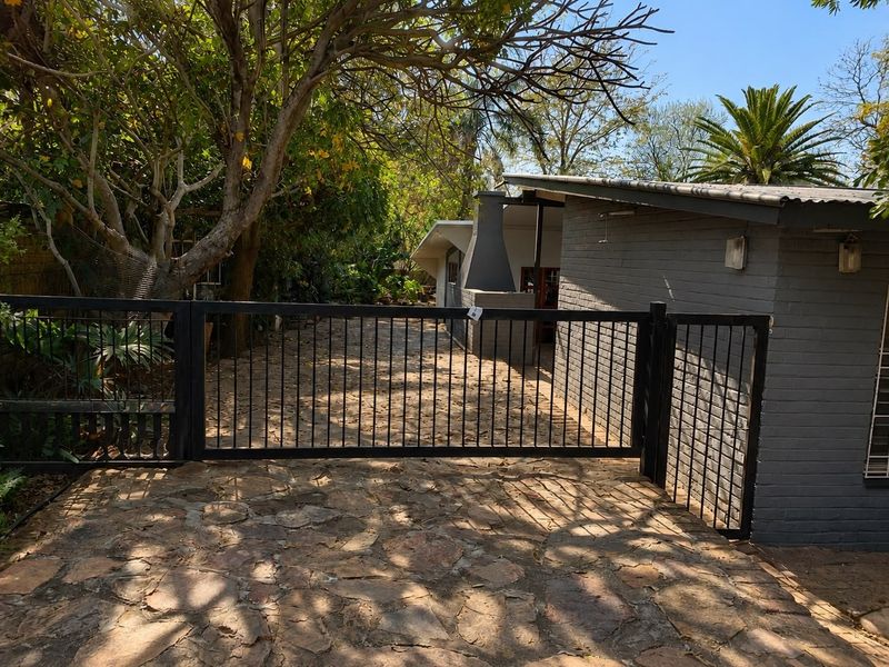 Rear exterior view featuring stone paving, a metal security gate, and a built-in outdoor fireplace adjacent to a brick-walled structure.