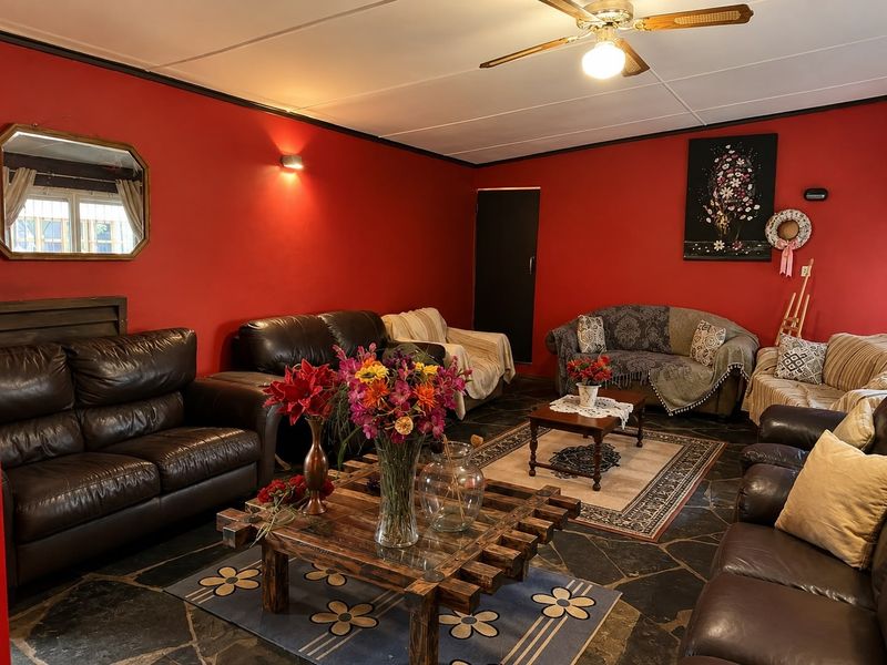 A spacious living room featuring dark stone tile flooring, a ceiling fan, and bold red walls, offering a traditional layout.
