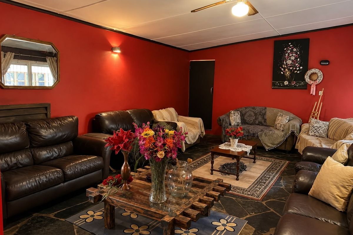 A spacious living room featuring dark stone tile flooring, a ceiling fan, and bold red walls, offering a traditional layout.