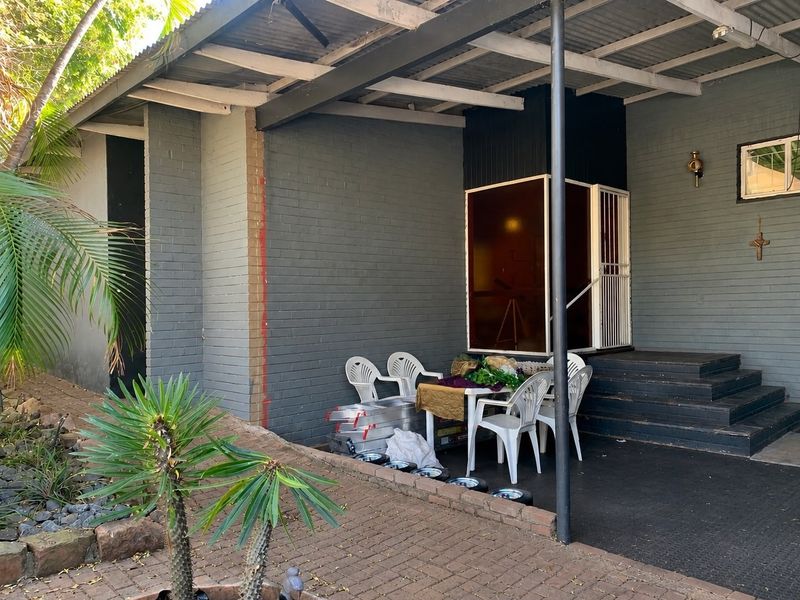 A covered outdoor patio area featuring painted brick walls, a raised timber deck, and a paved ground surface, providing a functional space for outdoor living.