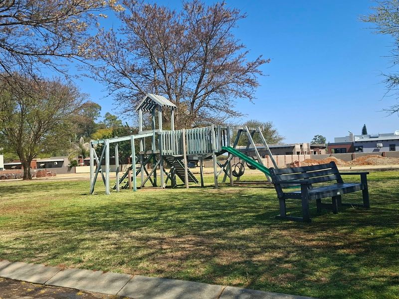 A well-maintained communal garden area featuring a wooden playground structure and a park bench set within a grassy landscape.