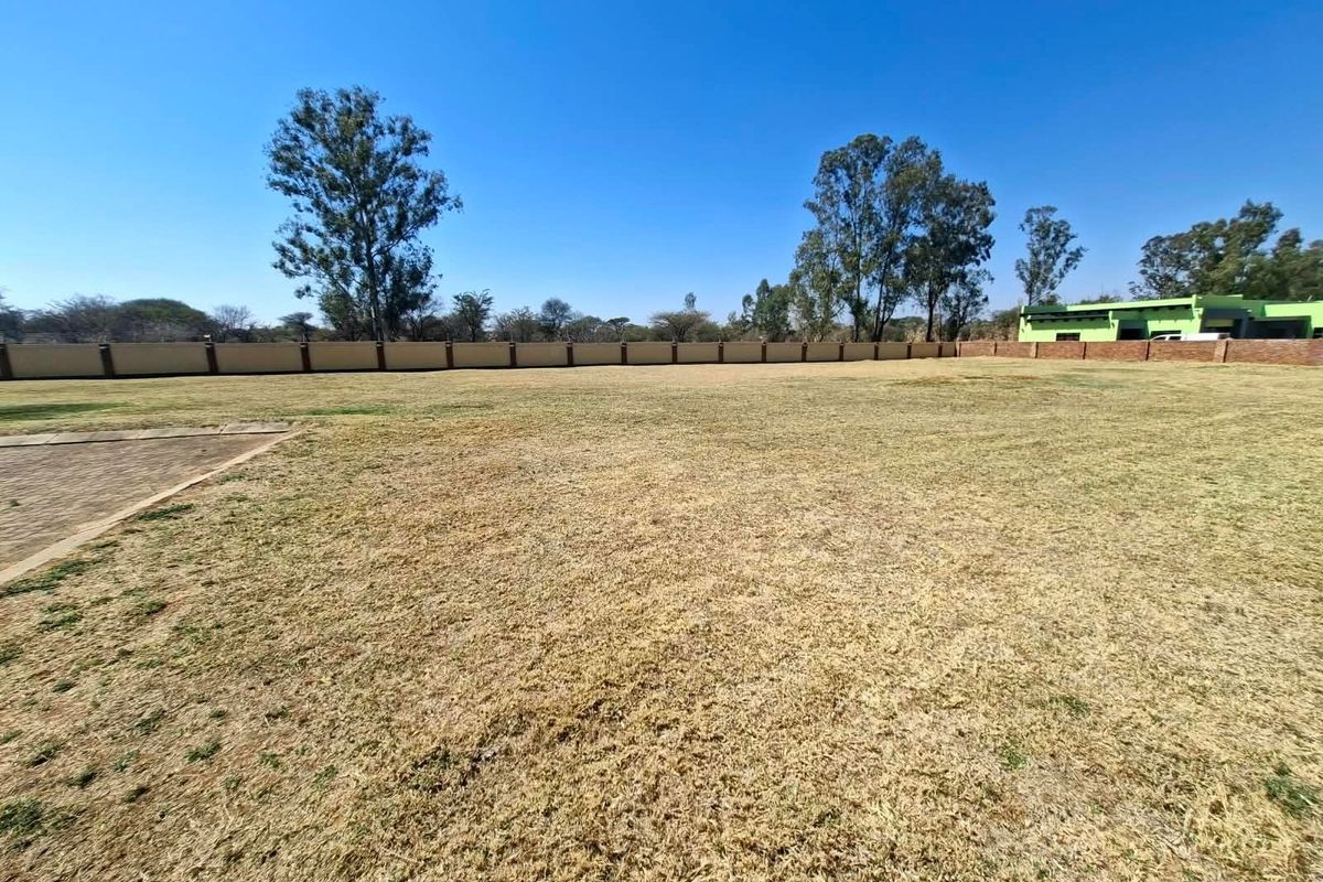 A spacious, level residential plot featuring a perimeter wall and established grass, offering a clear area for potential development.