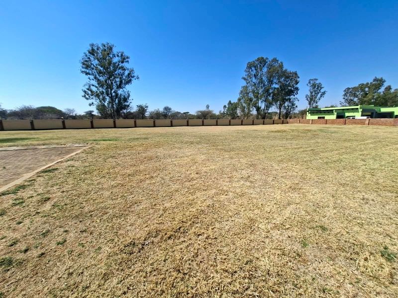 A spacious, level residential plot featuring a perimeter wall and established grass, offering a clear area for potential development.