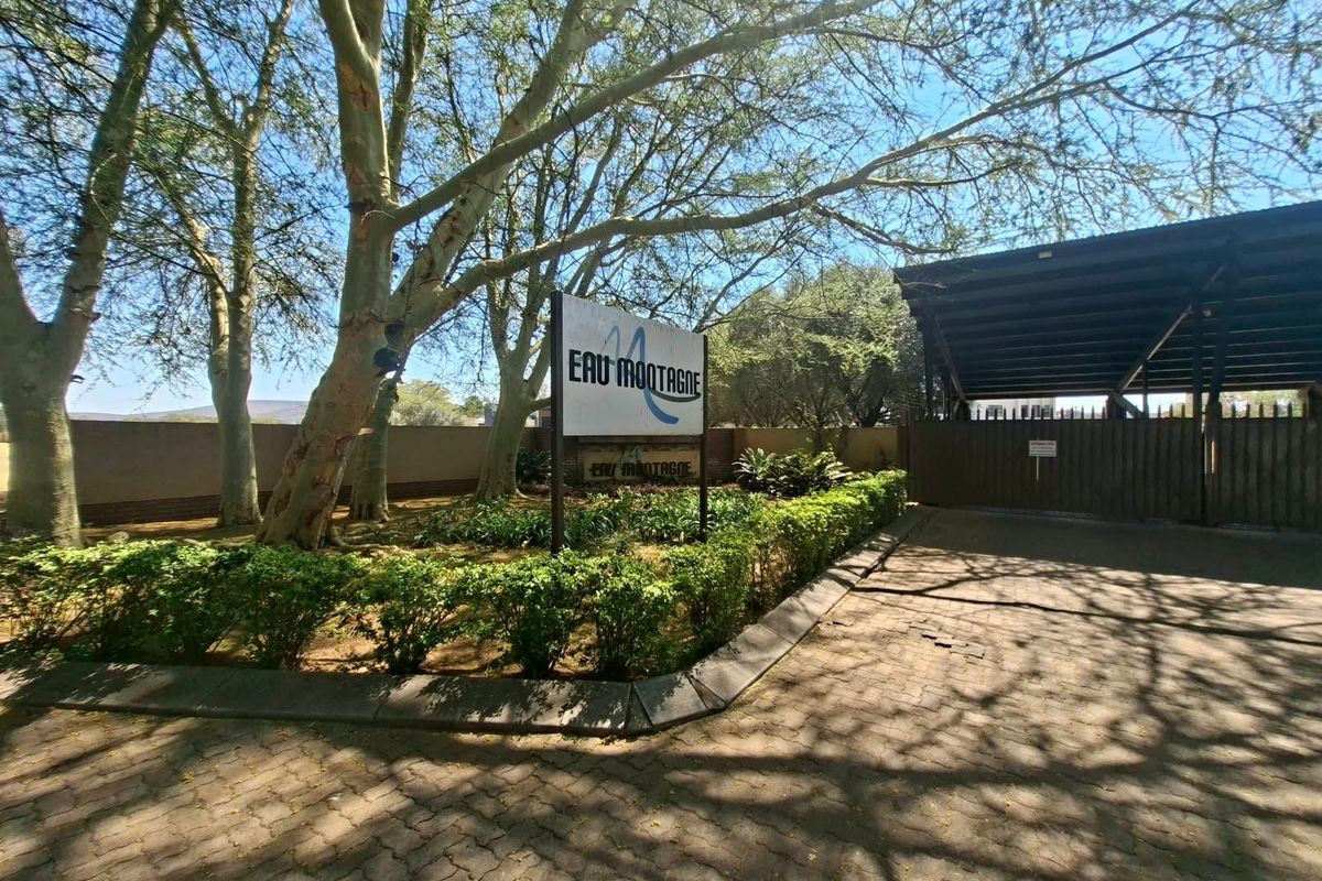 Entrance view of the property featuring a paved driveway, security gate, and established landscaping with mature trees and signage.