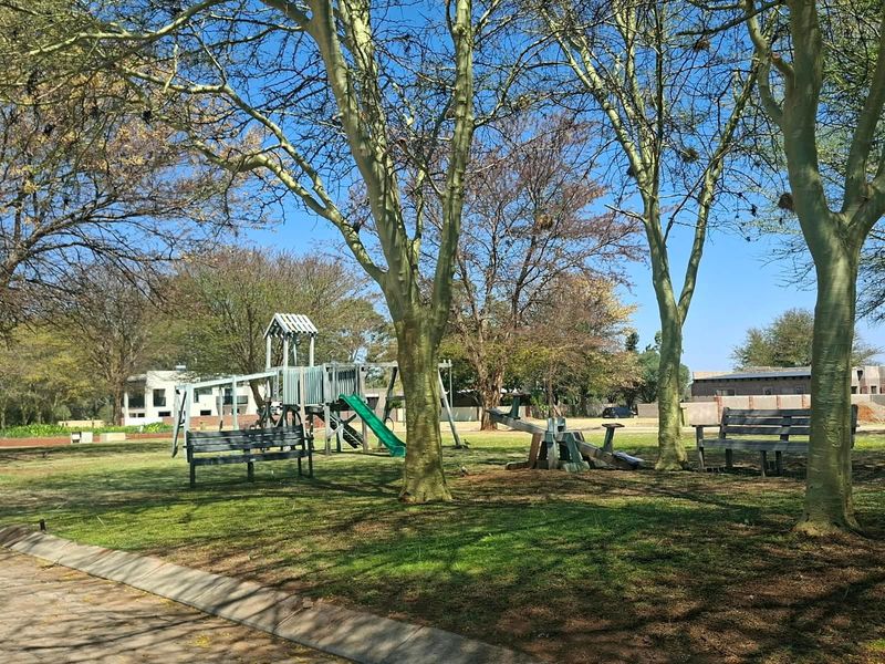 A well-maintained communal garden area featuring mature trees, park benches, and playground equipment, providing a pleasant outdoor space for residents.