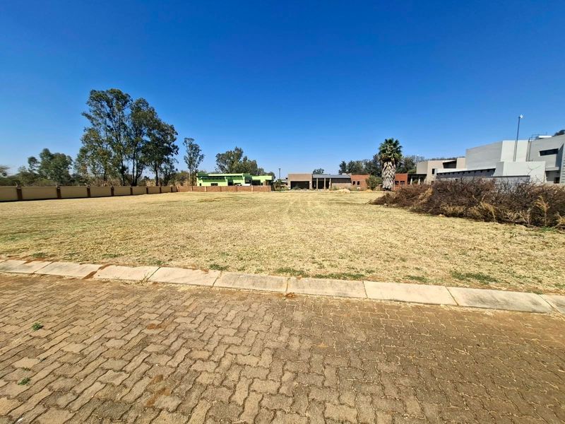 A vacant residential plot featuring a level grassed surface, paved street frontage, and established perimeter walling in a developed estate setting.