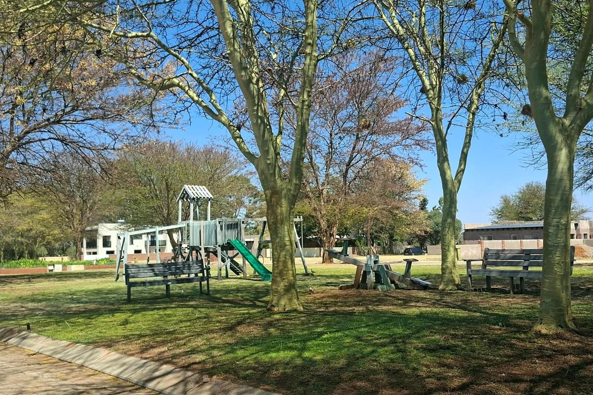 A well-maintained communal garden area featuring mature trees, park benches, and playground equipment, providing a pleasant outdoor space for residents.