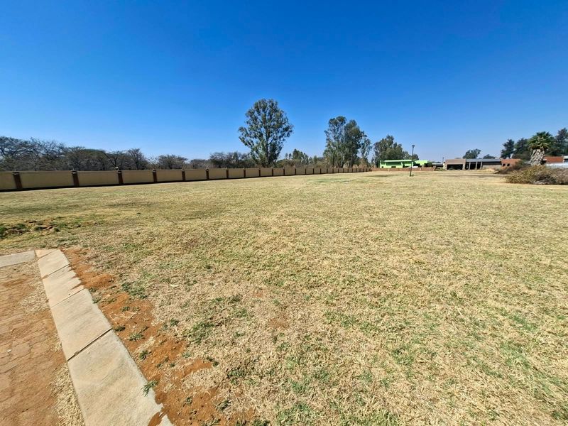 A spacious, level vacant residential plot featuring a perimeter wall and established grass, offering a blank canvas for future development.
