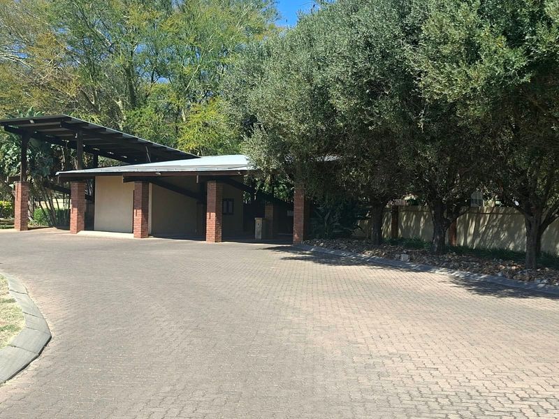 A well-maintained front entrance area featuring a paved driveway, covered parking structure with brick pillars, and mature trees providing shade.
