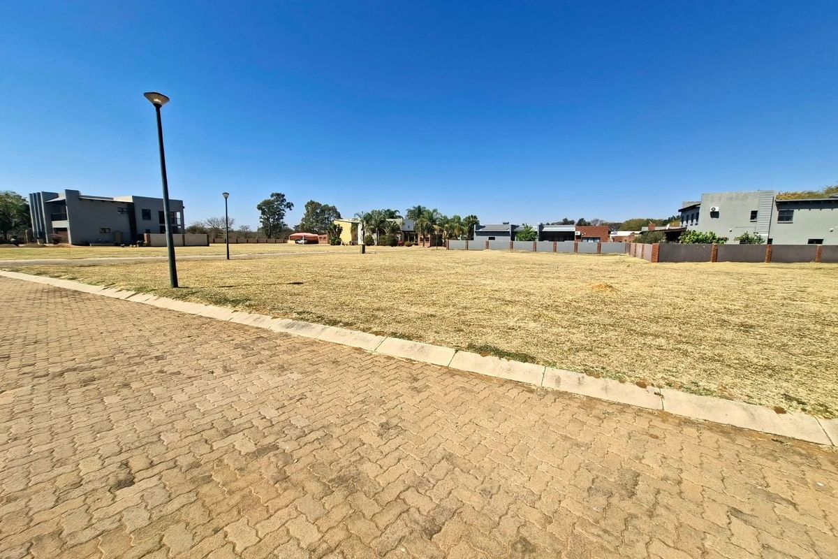 A vacant residential plot featuring paved street access, concrete curbing, and established street lighting in a developed estate setting.