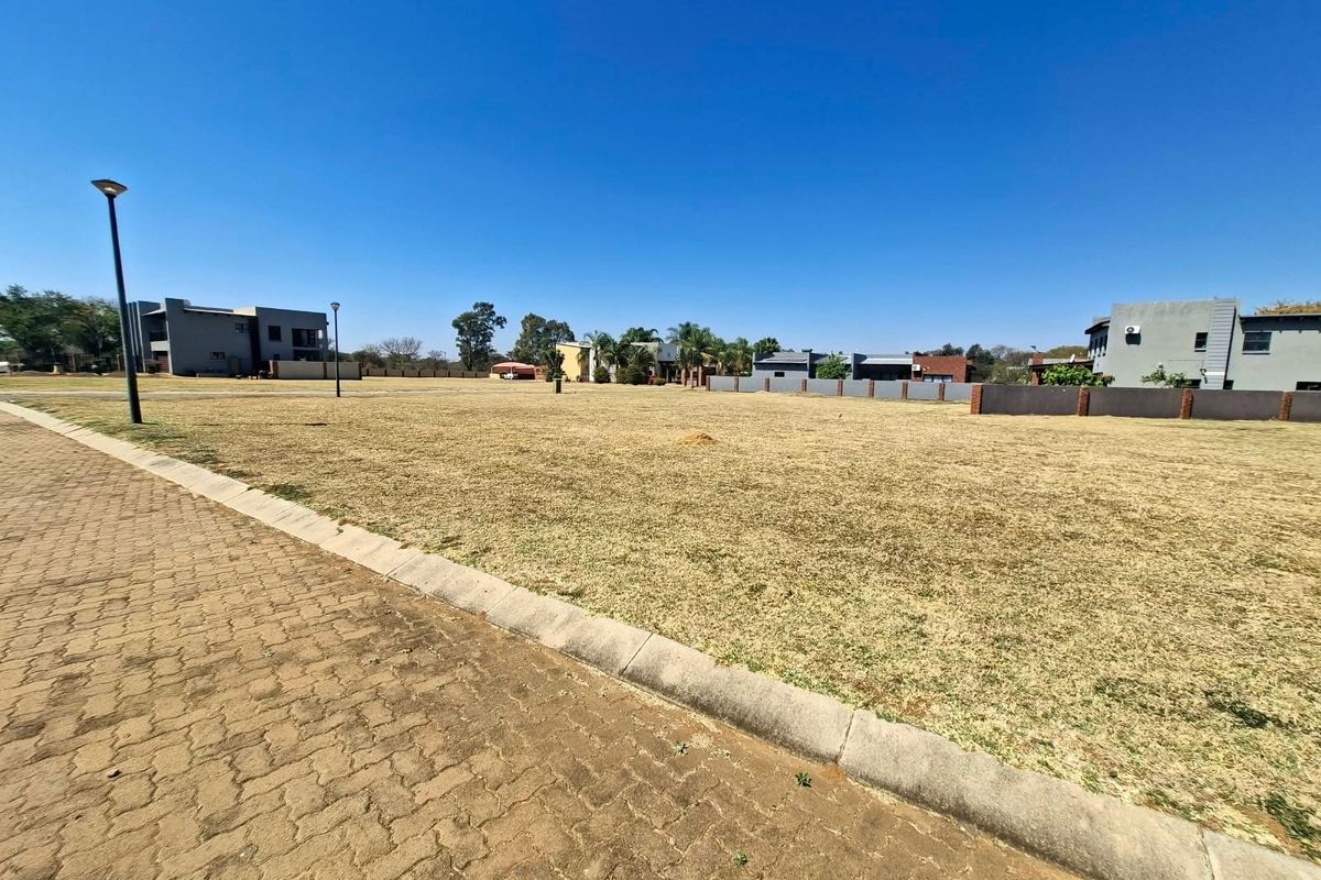 A vacant residential plot featuring a paved driveway, concrete curbing, and established street lighting in a developed neighborhood setting.