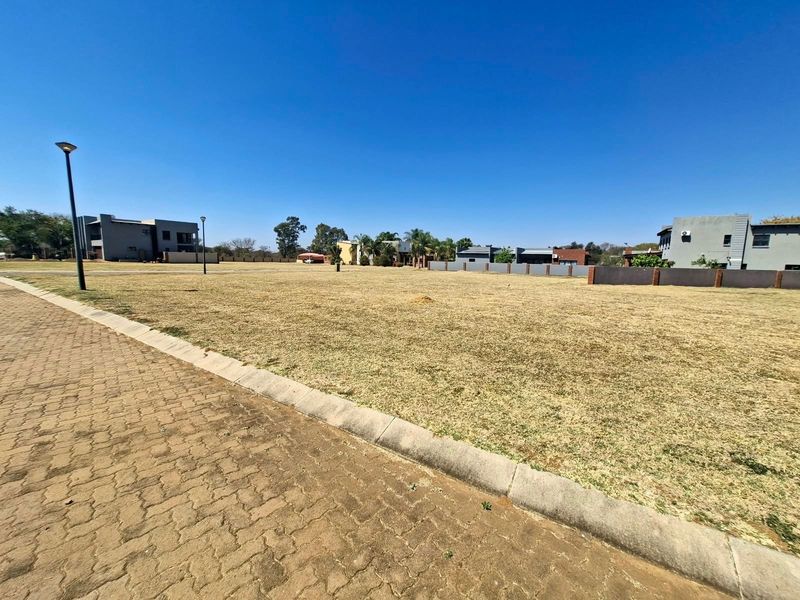 A vacant residential plot featuring a paved driveway, concrete curbing, and established street lighting in a developed neighborhood setting.