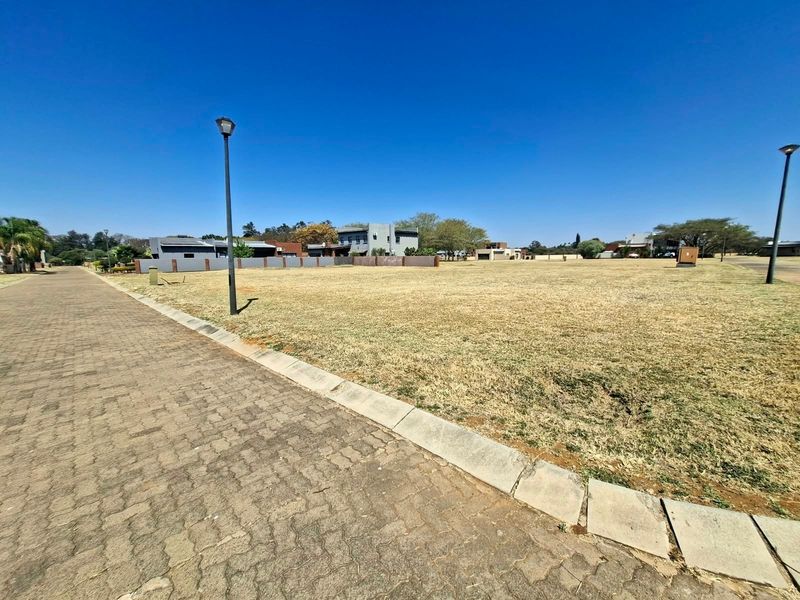 A vacant residential plot featuring established paving, street lighting, and concrete curbing, situated in a developed neighborhood setting.