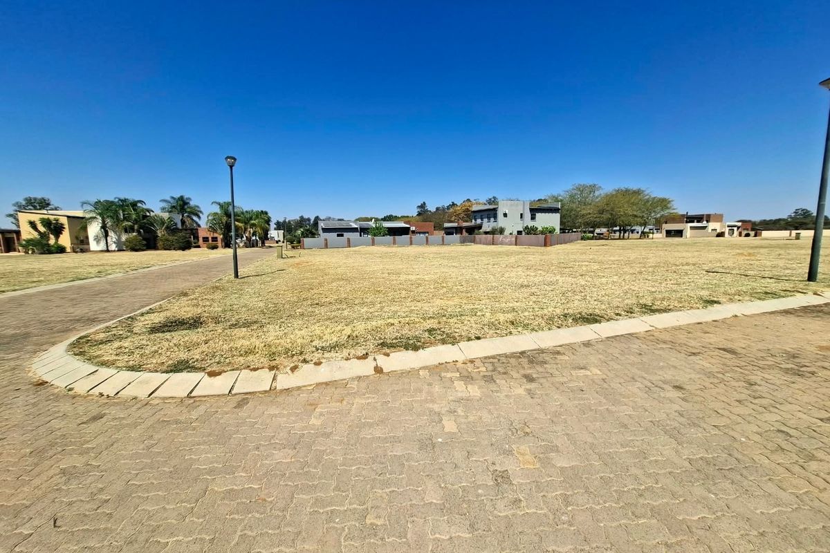 A vacant residential plot featuring established paving, kerbing, and street lighting, situated within a developed neighborhood setting.