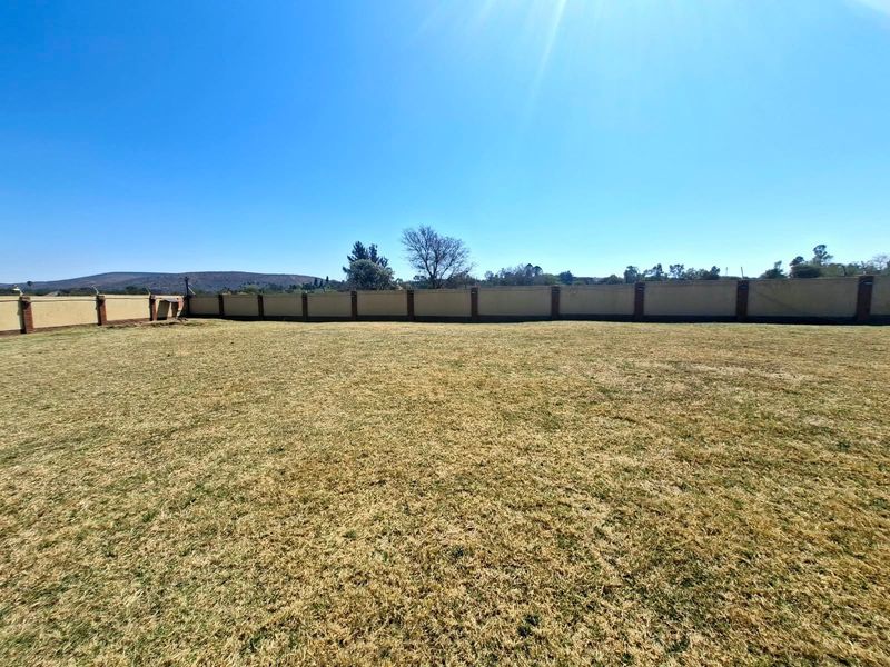A spacious, level residential plot featuring a well-defined perimeter wall with brick pillars and an expansive grass lawn.