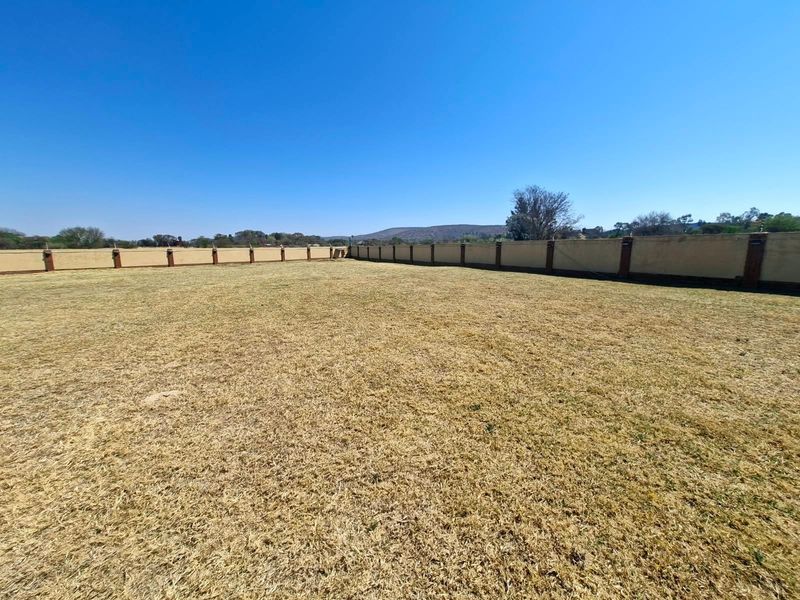 A spacious, level vacant residential plot enclosed by a perimeter wall with brick pillars, offering a clear canvas for development.