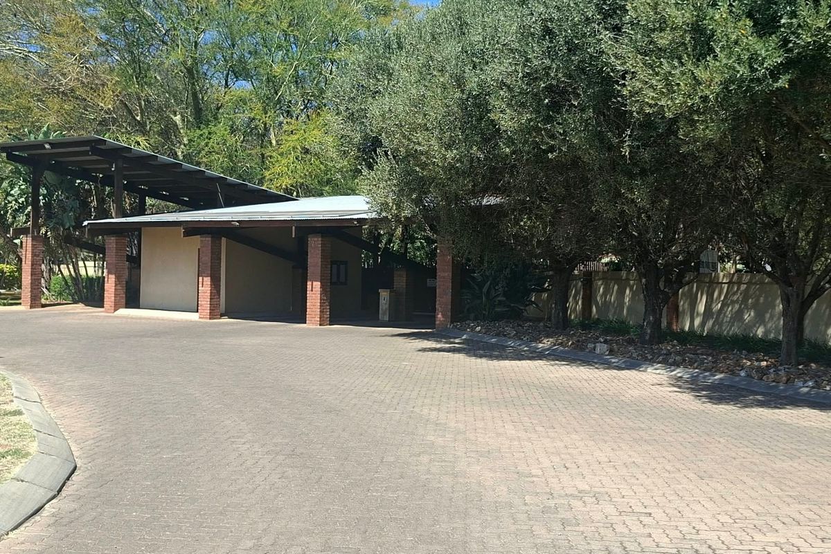 A well-maintained front entrance area featuring a paved driveway, covered parking structure with brick pillars, and mature trees providing shade.