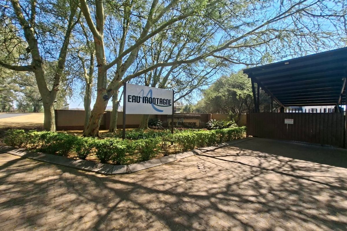 Entrance view of the Eau Montagne residential estate featuring a paved driveway, security gate, and established garden landscaping.