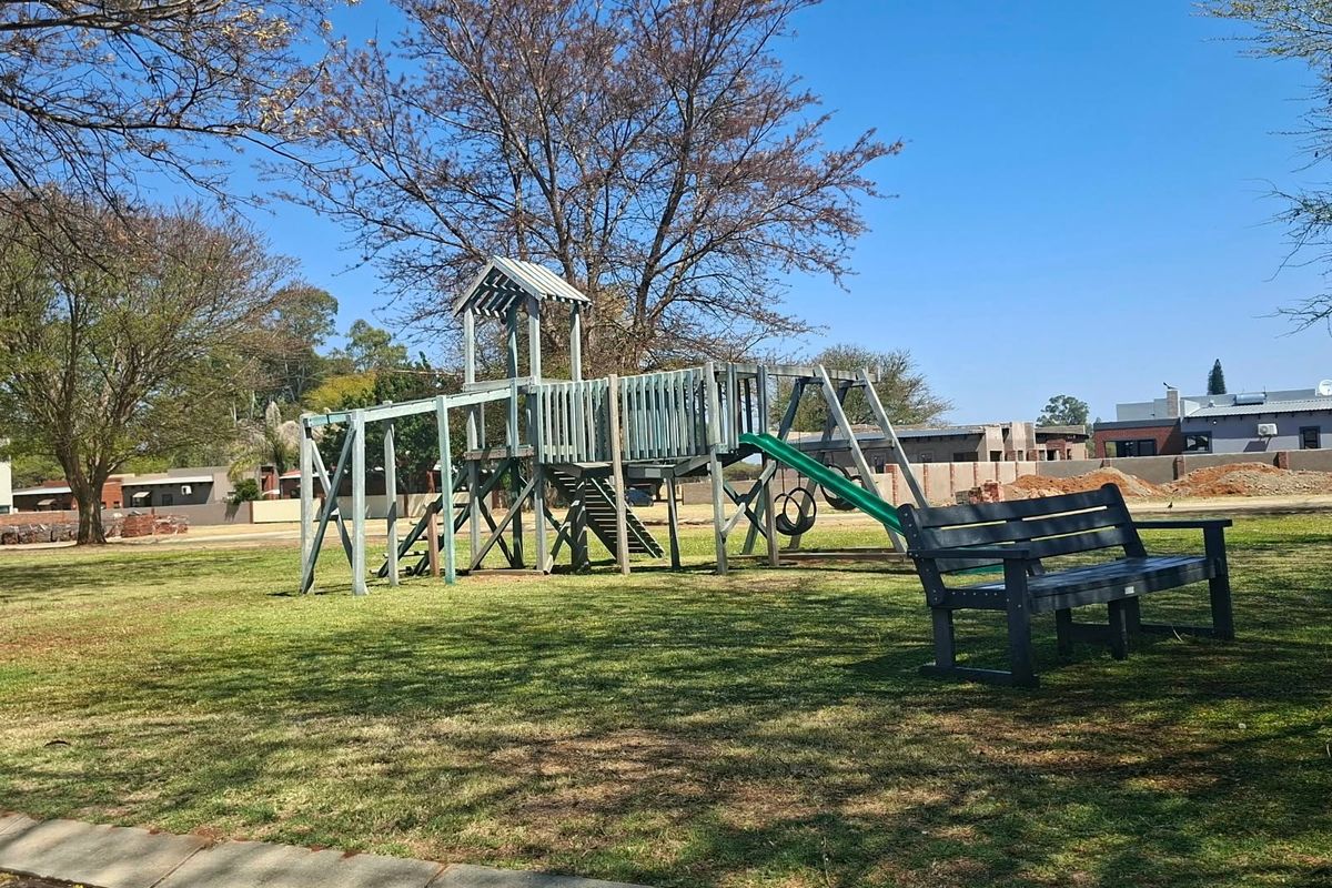 A well-maintained communal garden area featuring a wooden playground structure and a park bench set within a grassy landscape.