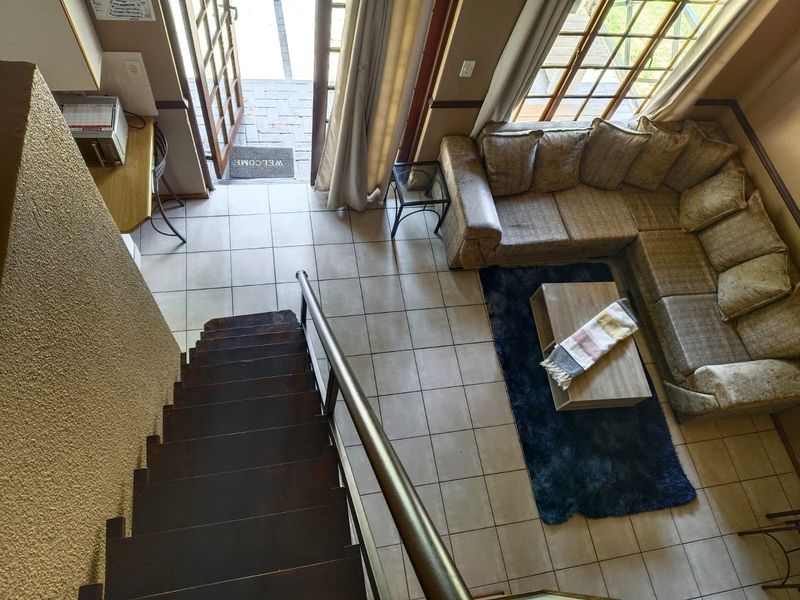 Open plan living area featuring tiled flooring, a wooden staircase with metal handrail, and direct access to the outdoor patio through french doors.