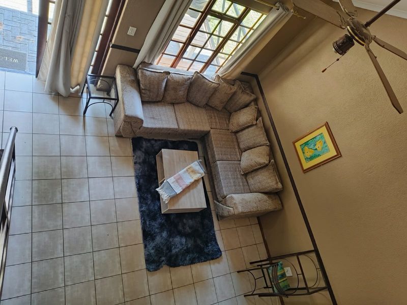 A high-angle view of a living room featuring tiled floors, a ceiling fan, and large windows providing natural light and access to the patio.