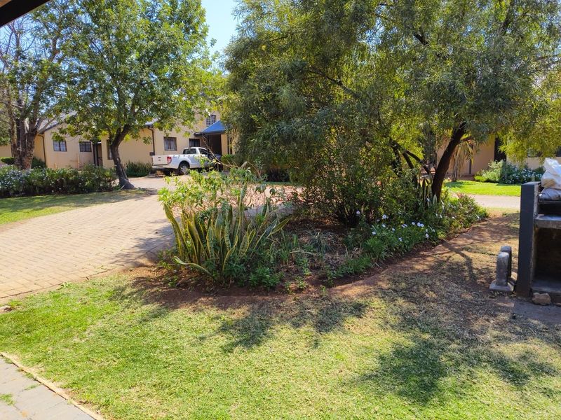 Front exterior view of the townhouse featuring a paved driveway, established garden, and a built-in outdoor braai area.