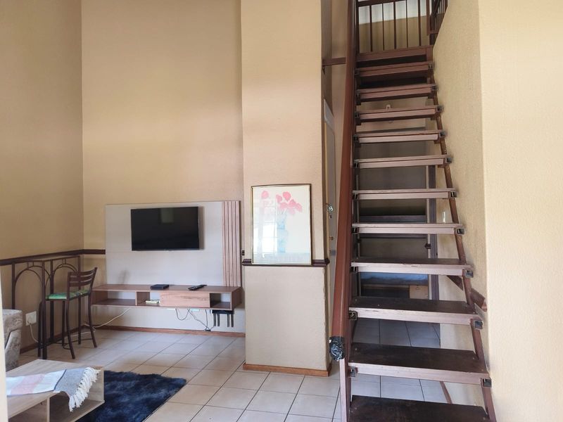 Living area featuring tiled flooring, a built-in media console, and an open-tread staircase leading to the upper level.