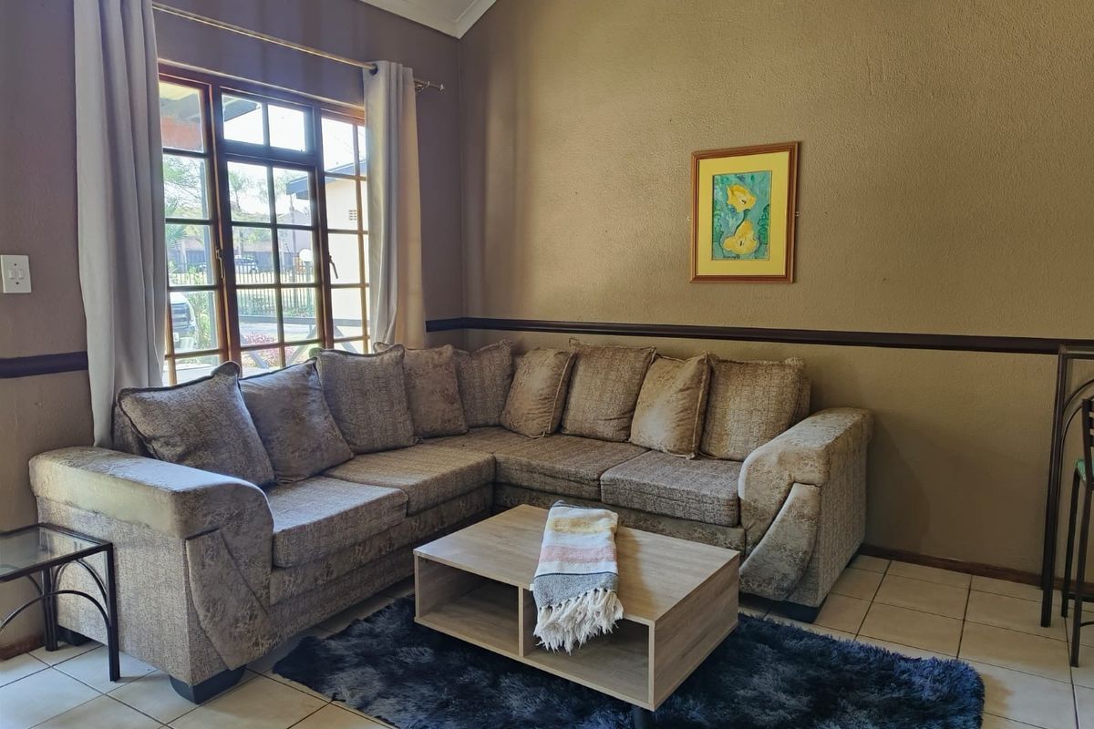 A cozy living room featuring tiled flooring, a vaulted ceiling, and a large window that allows for natural light.