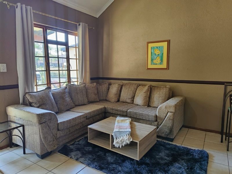 A cozy living room featuring tiled flooring, a vaulted ceiling, and a large window that allows for natural light.