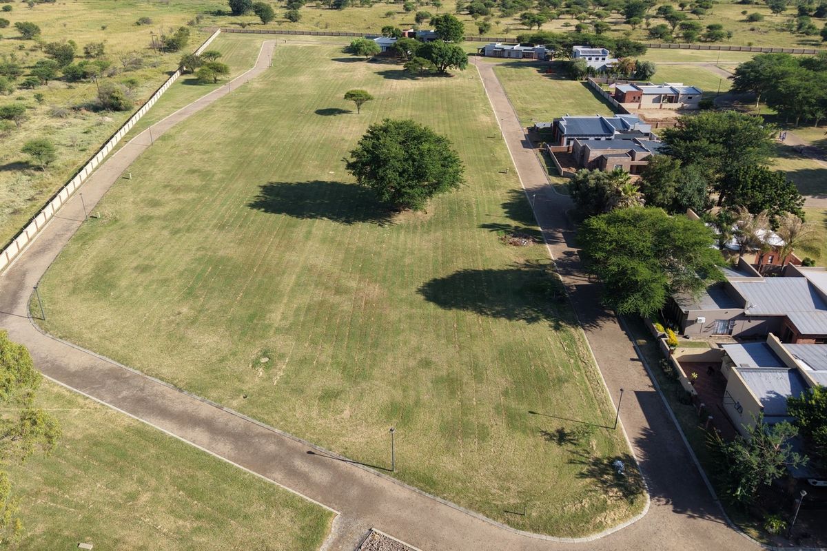 Aerial view of a large, well-maintained vacant residential plot featuring established trees, perimeter fencing, and paved access roads within a residential estate.